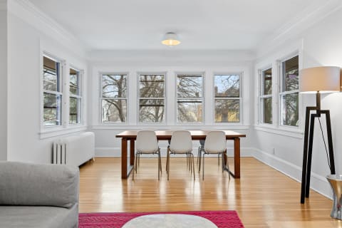 A modern dining area featuring a wooden table, white chairs, and bright windows.