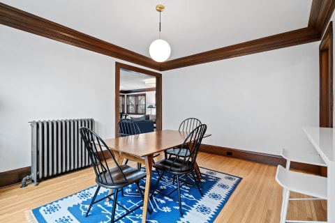 Dining room with wooden table, black chairs, blue rug, and vintage radiator.