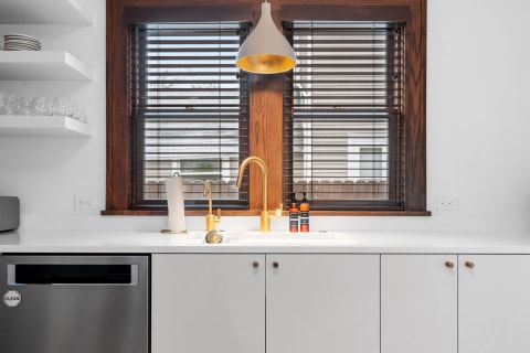 A serene kitchen scene showcasing a golden faucet, wooden window frames, and modern cabinetry.