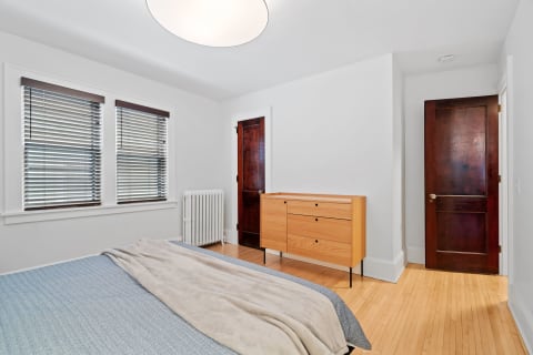 A bright bedroom with wooden details, a blue blanket on the bed, and a wooden dresser.