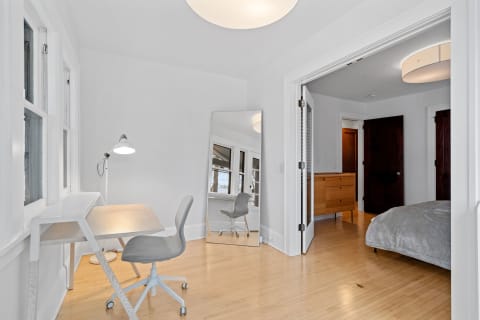 A minimalist home office area with a desk, a chair, and a mirror, adjacent to a bedroom entrance.