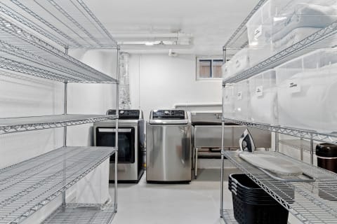 Interior of a clean laundry room featuring metal shelves, washing machines, and storage containers.