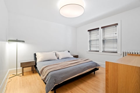 A clean and modern bedroom with a bed, nightstand, floor lamp, and wooden flooring.