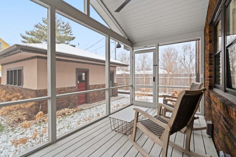 Screened porch with rocking chairs and a view of an outbuilding in winter.
