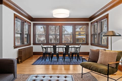 Interior of a stylish living room with a dining area, large windows, and modern furniture.