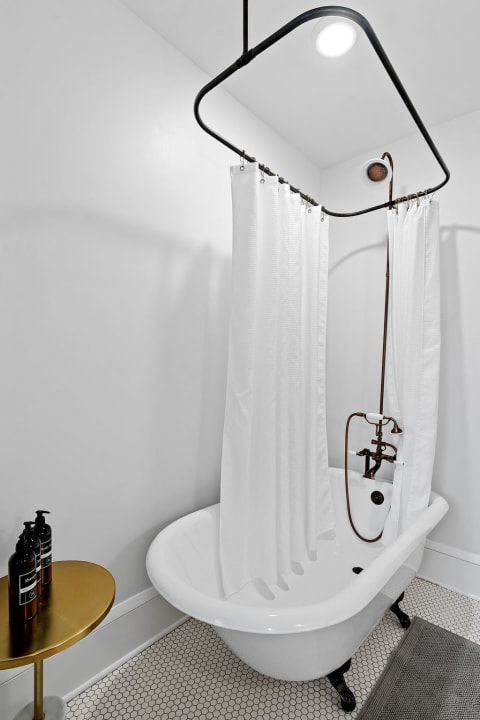 Vintage bathroom with a freestanding white tub, black fixtures, and a gold side table.