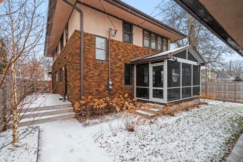 Two-story house with brick and stucco exterior, side view showing a screened porch and snowy surroundings.