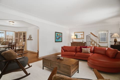 A spacious living room featuring a rust leather sofa, wooden coffee table, and decorative artwork.