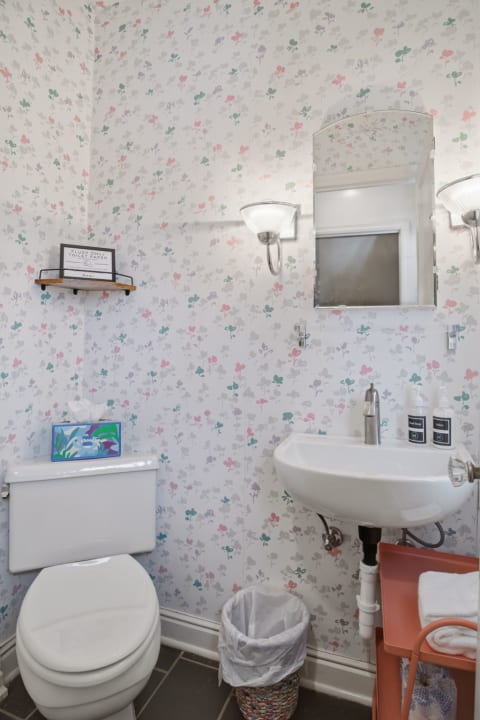 A cozy powder room decorated with pastel floral wallpaper, featuring a modern sink, a toilet, and decorative accessories.