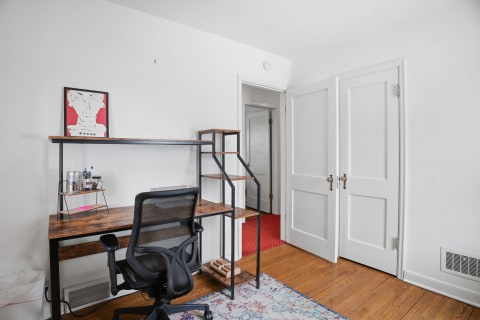 A modern desk setup in a bright room with an abstract art piece, ergonomic chair, and ladder-style shelving.