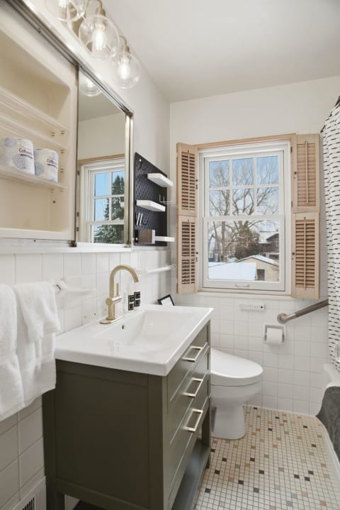 Modern bathroom with white subway tiles, olive green vanity, and charming shutters.