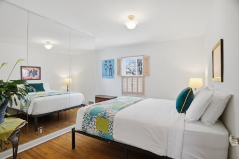 Bright bedroom featuring a bed with colorful linens, a green plant, and reflective sliding doors.
