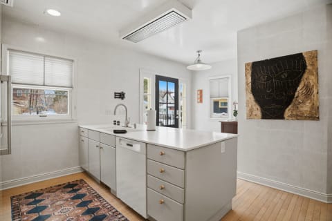 A modern kitchen with white cabinetry, a colorful rug, and an abstract face painting on the wall.