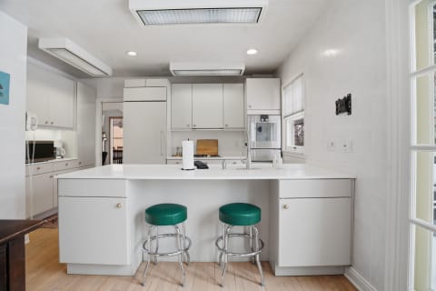 Modern white kitchen featuring a central island, green bar stools, and built-in appliances.