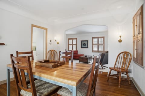 Cozy dining area with a wooden table and wooden chairs, leading to a bright living room with a red sofa.