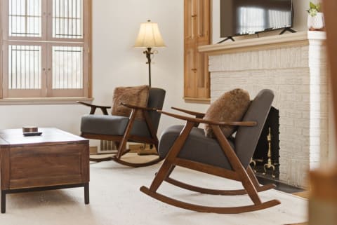 Cozy living room with mid-century rocking chairs, stone fireplace, and wooden coffee table.
