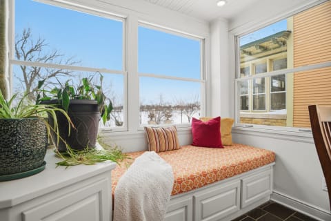 A cozy window seat with colorful cushions and green plants, offering a view of a snowy landscape outside.