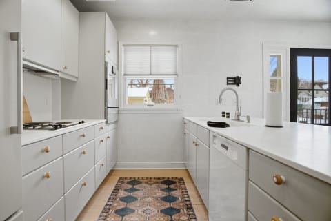 A contemporary kitchen featuring white cabinetry, stainless steel appliances, and a patterned rug.