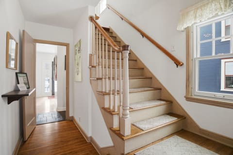 A warm wooden staircase in a bright entrance hall with a small console table and natural light coming through a window.
