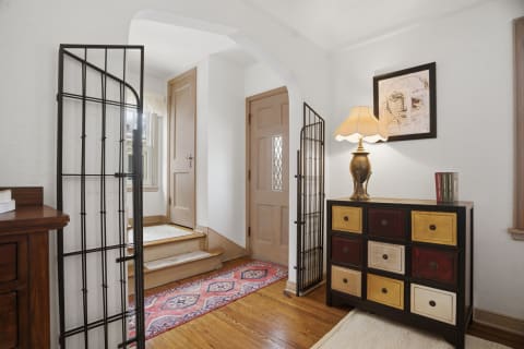 An elegant foyer featuring hardwood floors, a decorative chest of drawers, and an artistic wall hanging, bathed in soft light.