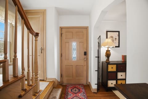 A welcoming foyer featuring wooden accents, a staircase, and a decorative lamp on a side table.