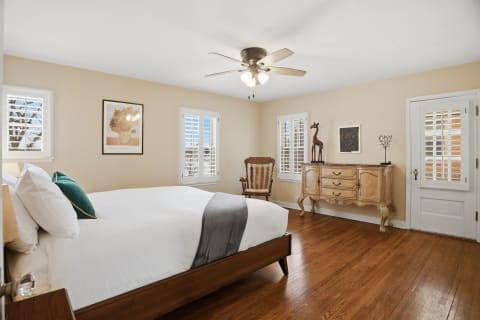 A serene bedroom with hardwood floors, vintage furniture, and natural light coming through plantation shutters.