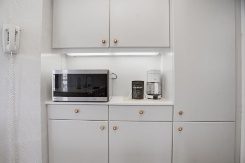 Modern kitchenette showcasing gray cabinets, a microwave, and a coffee maker against a textured white wall.