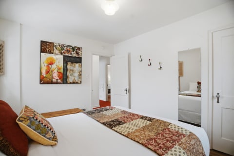 A cozy bedroom with white linens, a colorful quilt, and floral wall art.