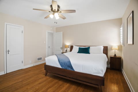 A serene bedroom with a wooden bed, white linens, and warm wood floors.