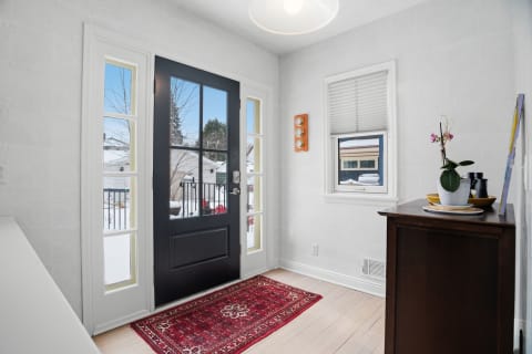 A bright entryway featuring a black front door, a red patterned rug, and natural light coming through the windows.