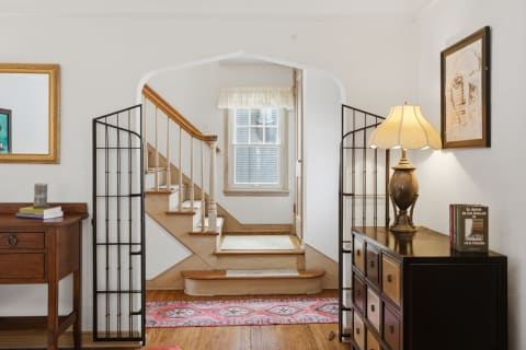 A cozy entrance with wooden floors, a console table, a decorative lamp, and a staircase leading up.