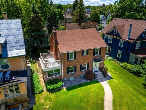 Two-story brick house with a curved pathway and lush landscaping in a residential area.