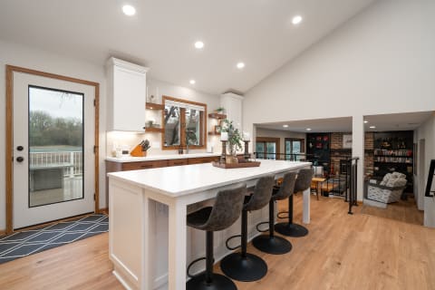 Modern kitchen with a white island and barstools, leading to an outdoor deck.