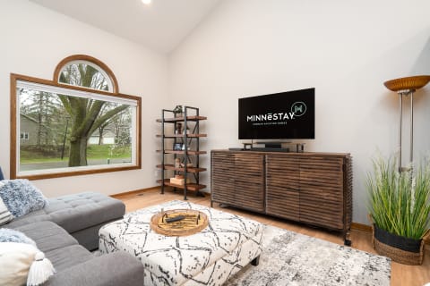 A modern living room with a gray sectional sofa, a TV, and a tall shelving unit.