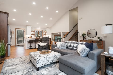 Cozy living room with gray sectional sofa, patterned ottoman, and light wooden accents in a modern home.