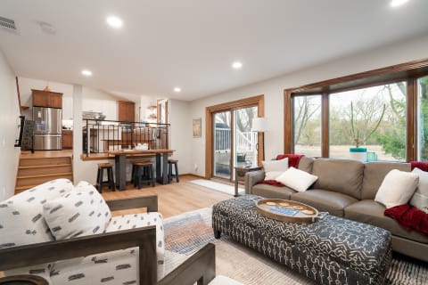 A modern living room featuring a gray sofa, patterned ottoman, and a kitchen area in the background.