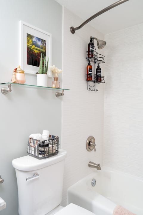 A stylish bathroom with a shower, decorative shelf, and organized toiletries.