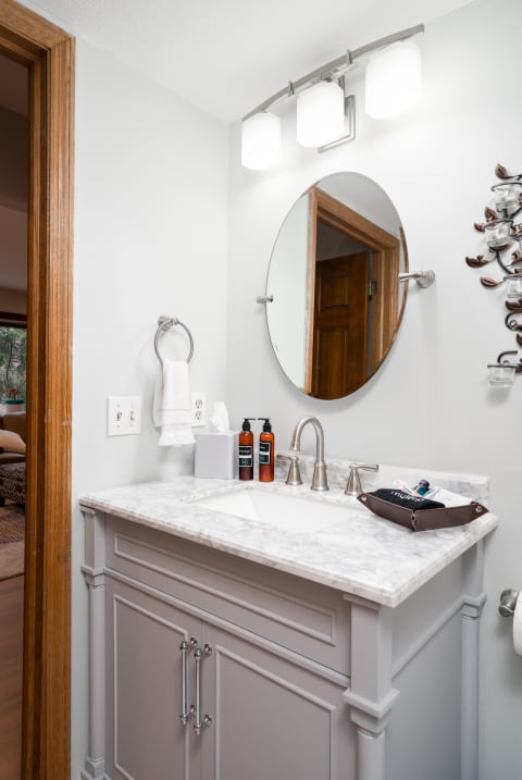 A stylish bathroom with a marble sink, circular mirror, and elegant lighting.