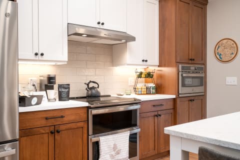 Interior view of a modern kitchen showcasing brown and white cabinetry, a stove, kettle, and fresh fruits in a basket.