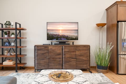 A contemporary living room with a flat-screen TV showing a sunset, a wooden cabinet, and decorative shelving.