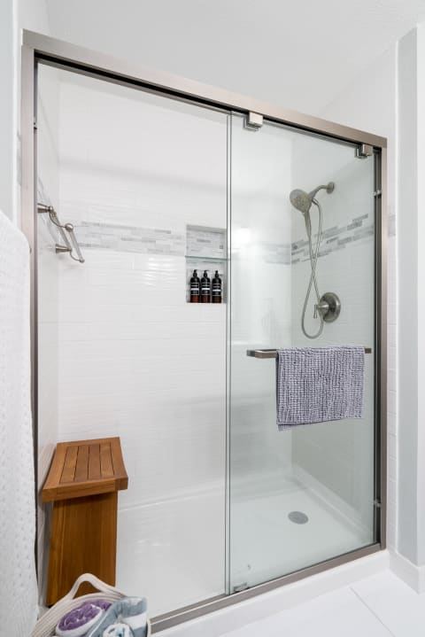 Modern shower design with glass doors, white tiles, and a wooden bench.