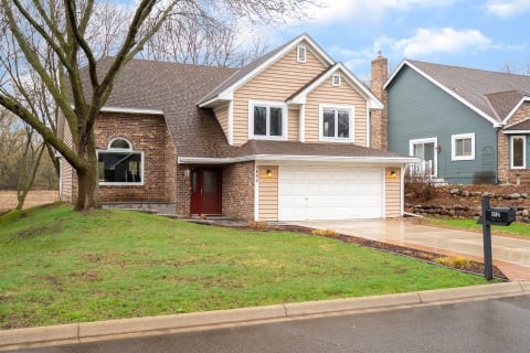 Front view of a two-story house with a brick and siding exterior, large windows, and a manicured yard.