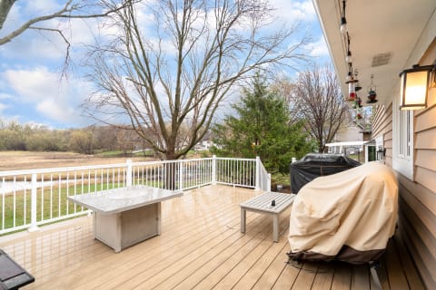 Outdoor deck with table, barbecue grill, and trees in the background beneath a cloudy sky.
