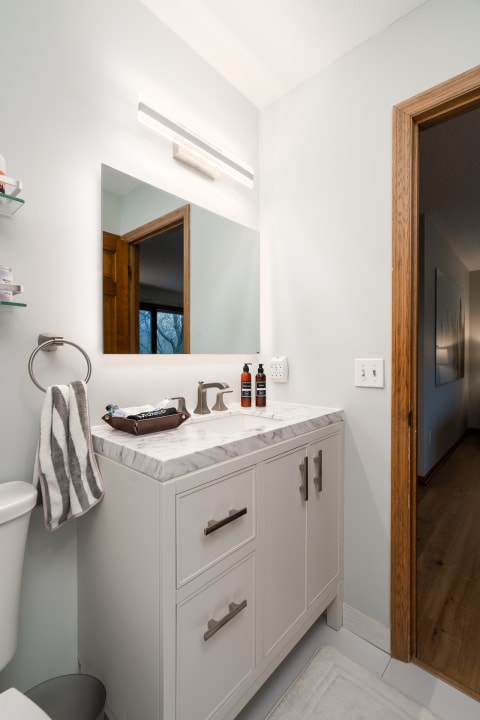 Modern bathroom with marble countertop, mirror, and light fixtures.
