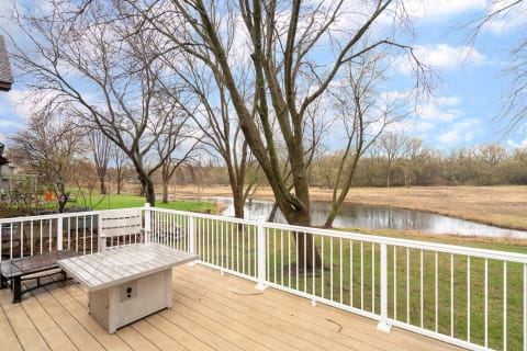 Outdoor deck with a table and bench overlooking a river and trees.