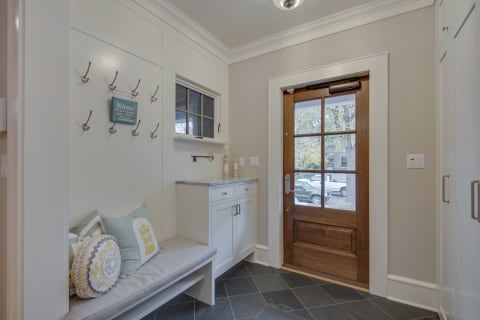 Your charming entryway welcomes you with built-in seating, hooks for coats, and a warm wooden door that opens to comfort.