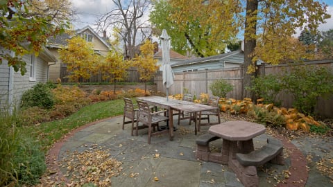 Outdoor dining space featuring a wooden table and chairs amidst autumn leaves and greenery.