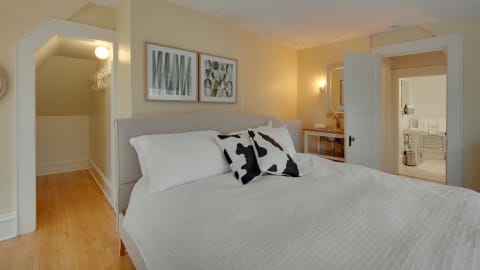 A serene bedroom featuring white linens, a black-and-white cow print pillow, and an open door leading to a bathroom.