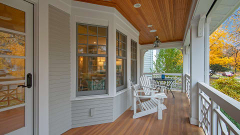 Cozy porch with white Adirondack chairs, warm wooden details, and autumn foliage in view.