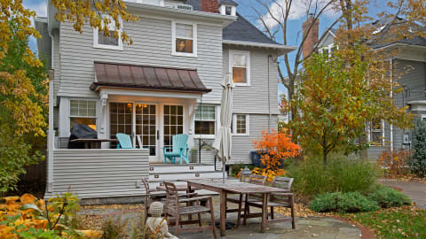 A gray house with a covered porch, outdoor seating, and colorful autumn foliage.